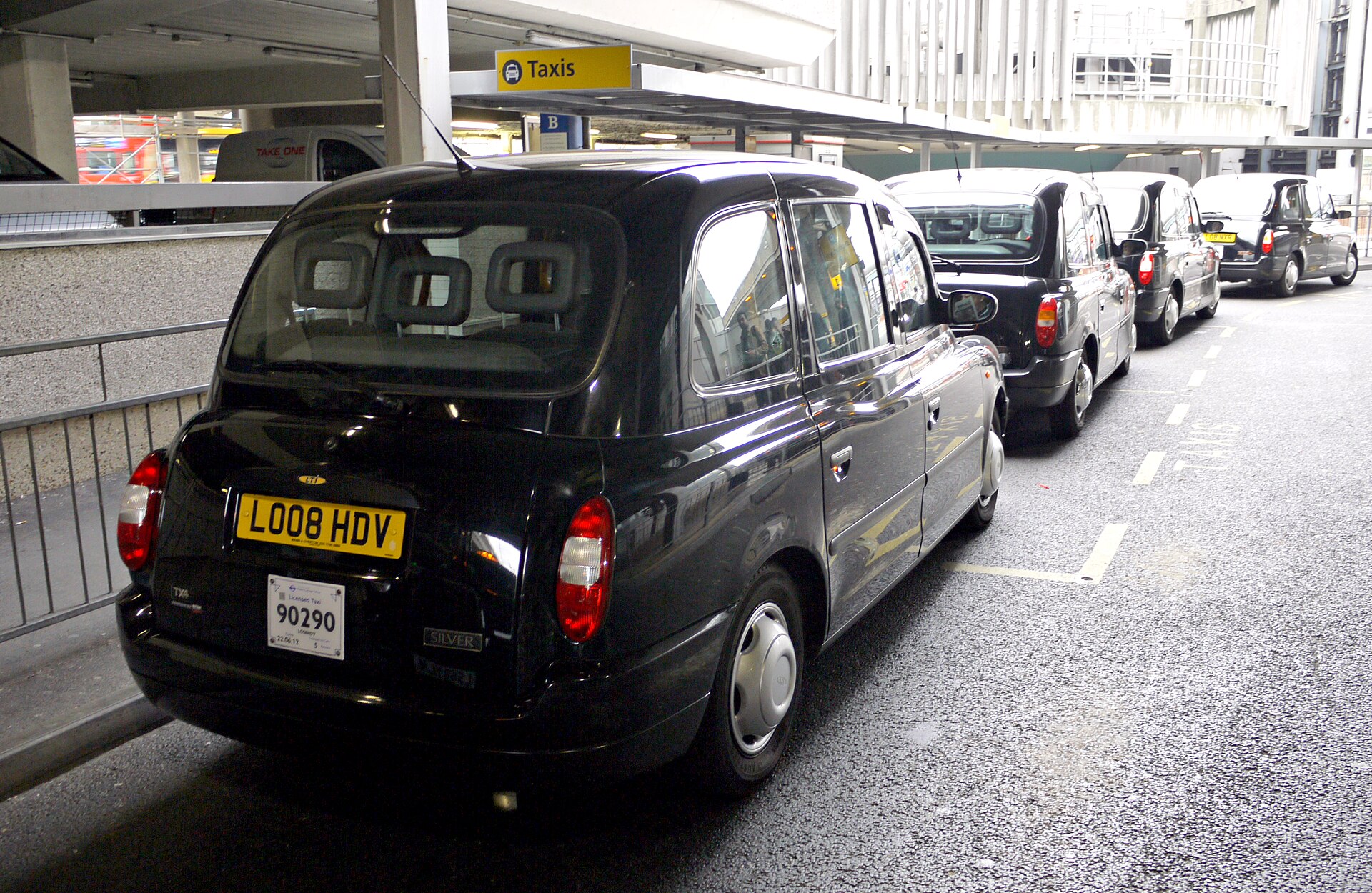 Black cabs queuing under a Taxis sign at Heathrow Airport's terminal pickup area.
