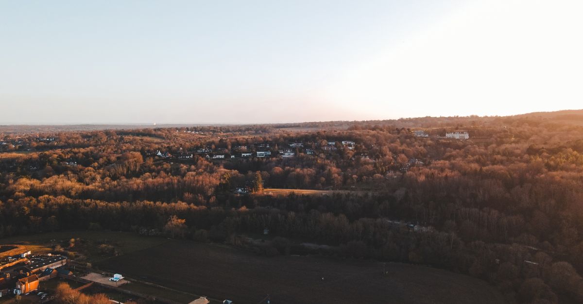 A scenic aerial shot over the English countryside at sunset showcasing houses and a vast forest.