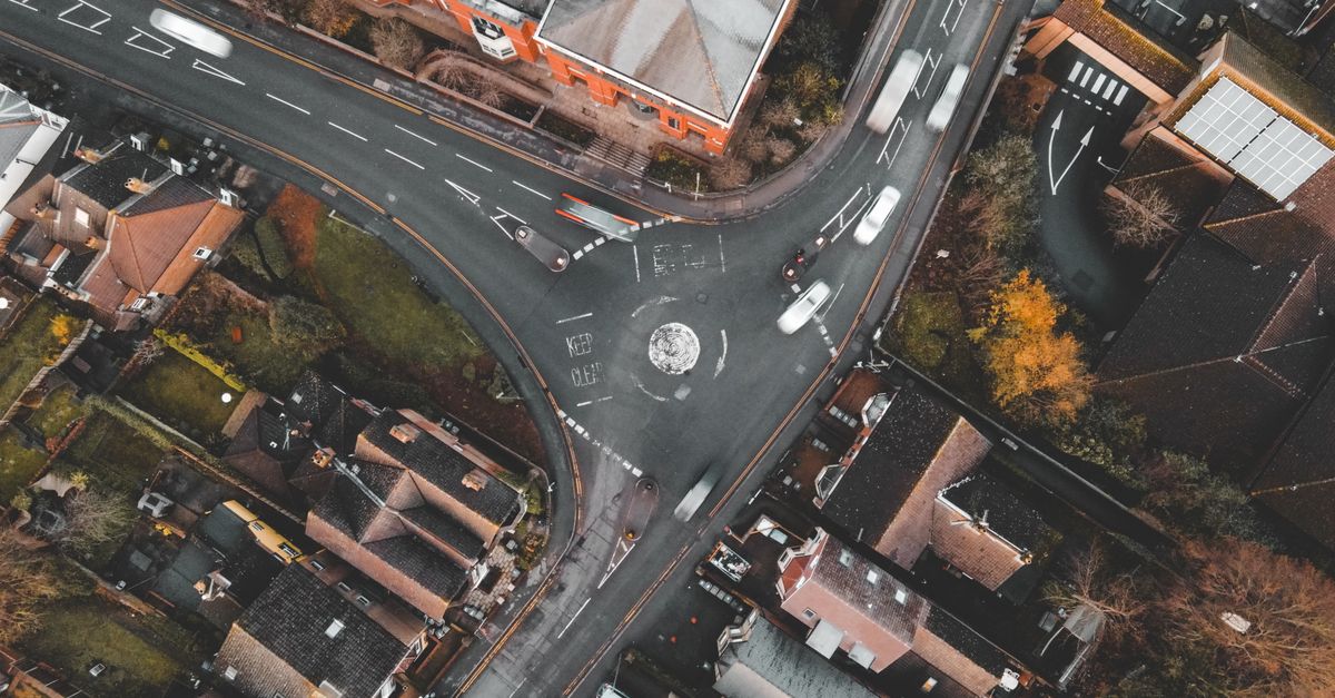 Aerial view of a large UK roundabout with 'keep clear' road markings surrounded by suburban houses.