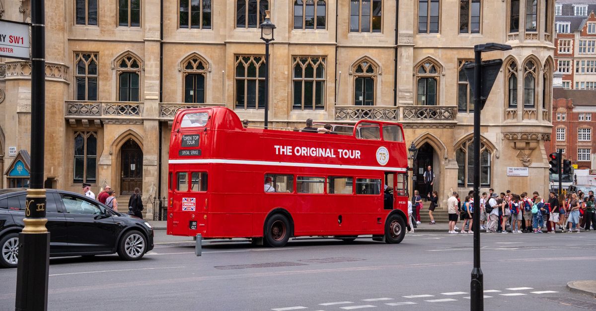 Vintage red double-decker bus offering tours in historic London with people nearby.