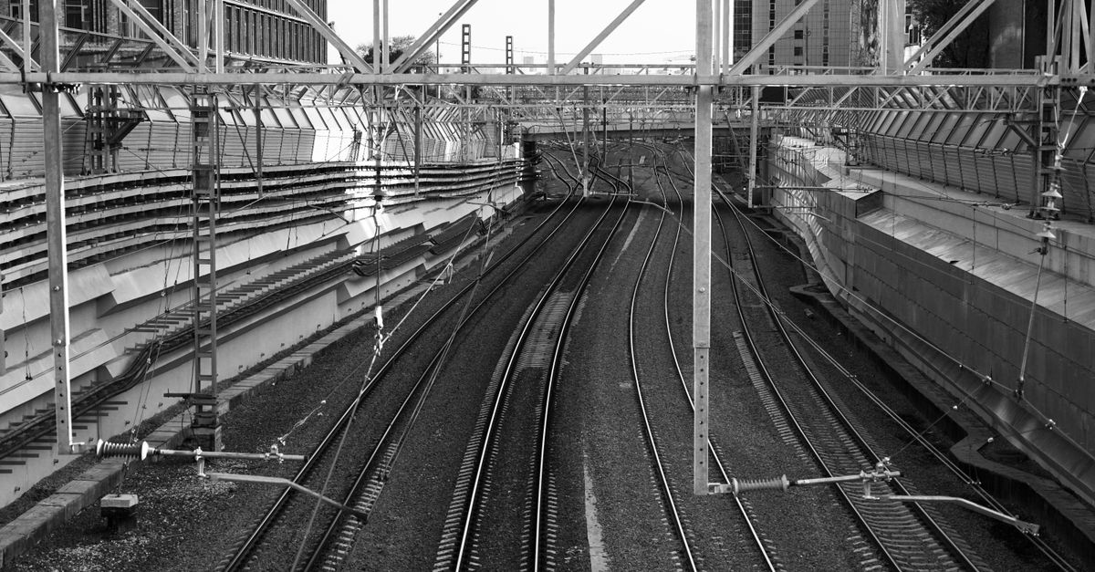 Black-and-white view of railway tracks curving away under overhead electrification gantries.