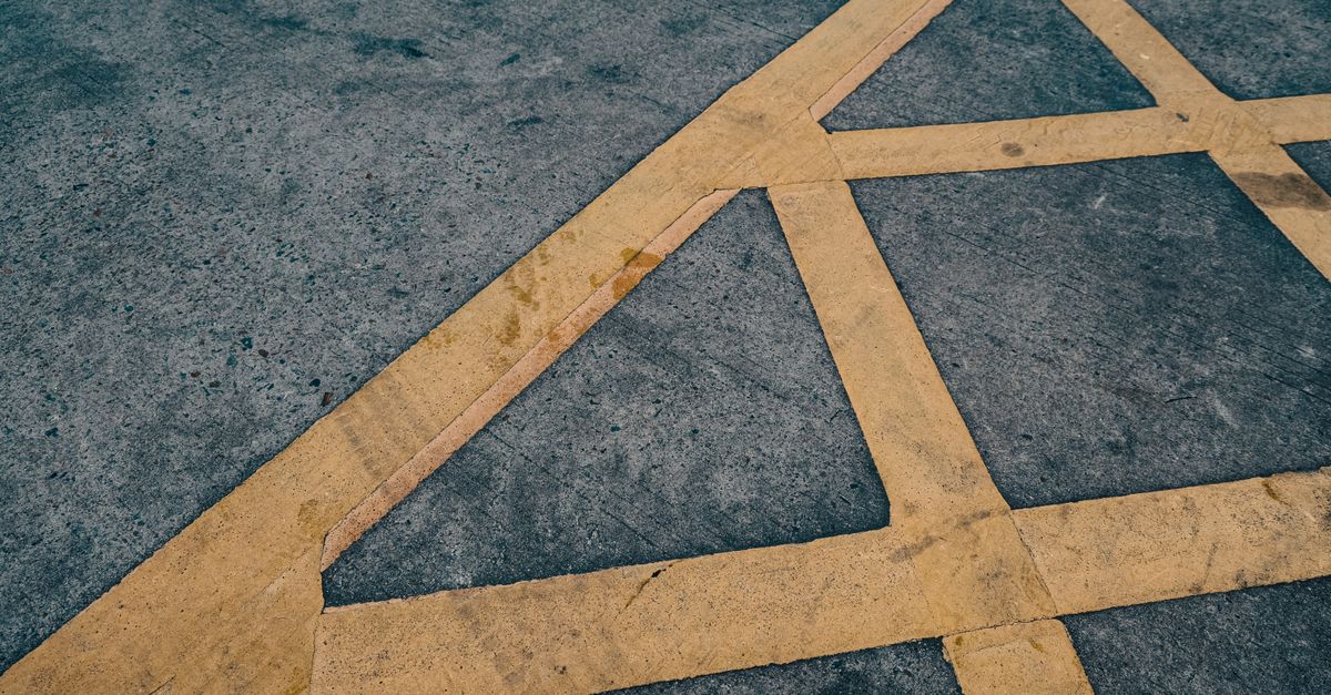 Abstract close-up of yellow hatched box-junction road markings on tarmac.