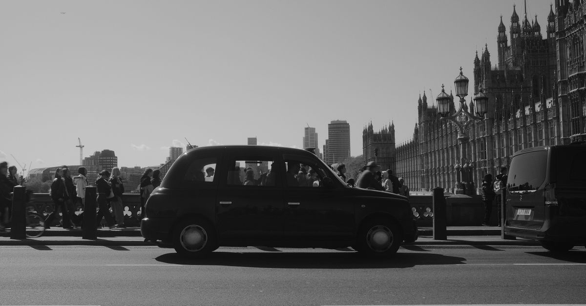 Black and white photo of a London black cab crossing Westminster Bridge with the Houses of Parliament behind.